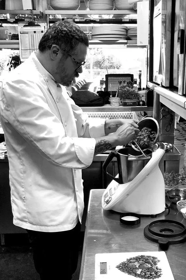 John Guerrero en chaquetilla de chef preparando una elaboración en una cocina profesional