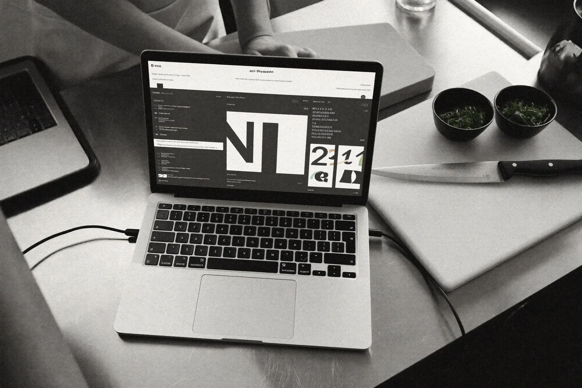 Laptop y mise en place sobre acero de cocina, fotografía editorial en blanco y negro